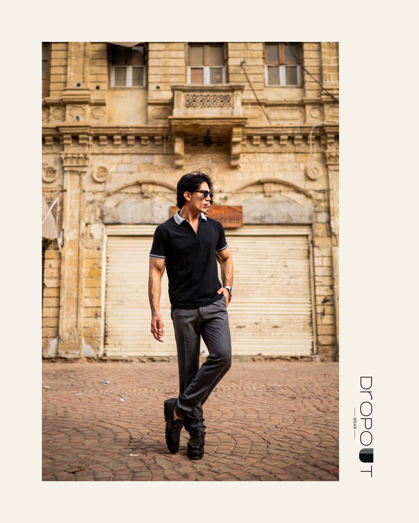 Man in black polo zipper shirt and jeans standing in front of a textured wall.